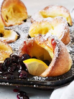 mini Dutch babies in muffin tin with lemons and blueberry sauce