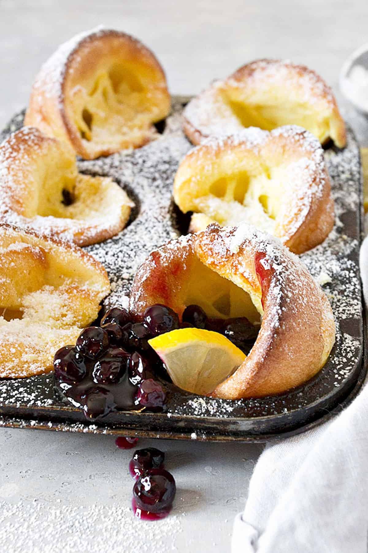 mini Dutch babies in muffin tin with lemons and blueberry sauce