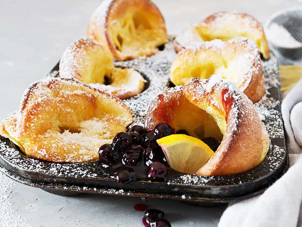 mini Dutch babies in muffin tin with lemons and blueberry sauce