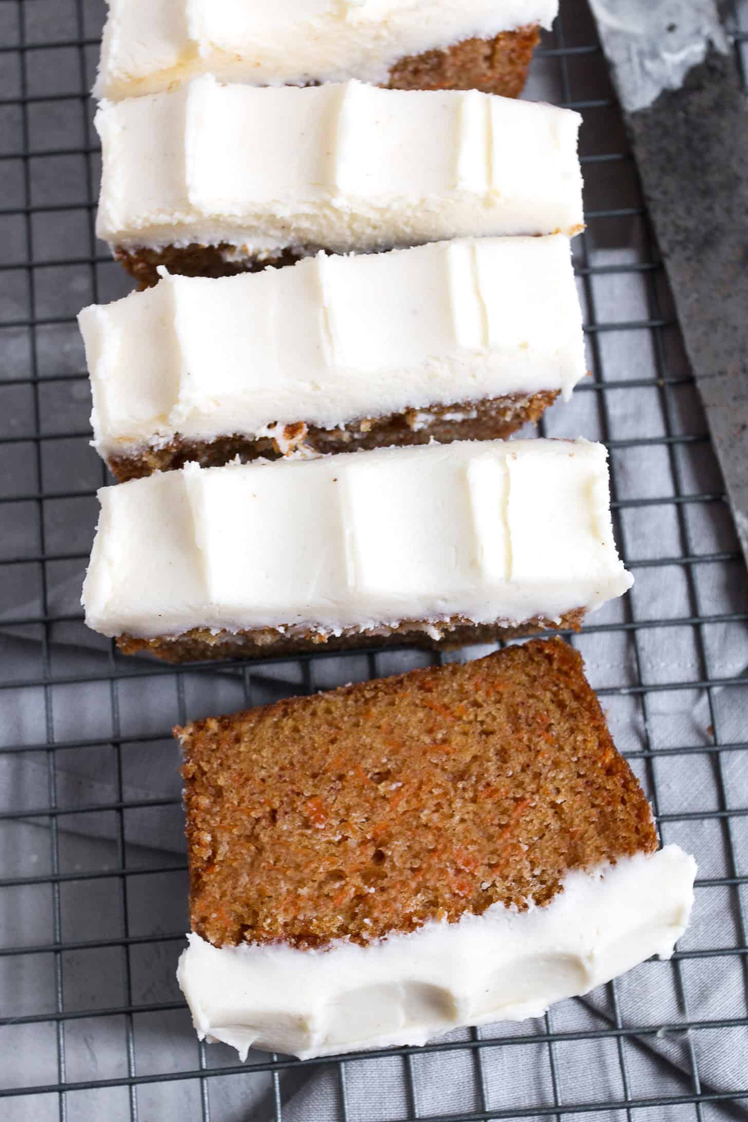 Carrot cake loaf with cream cheese frosting sliced on a cooling rack.