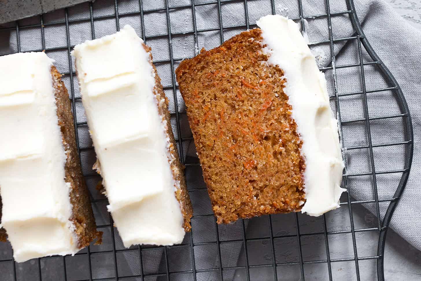 Carrot cake loaf with cream cheese frosting sliced on a cooling rack.