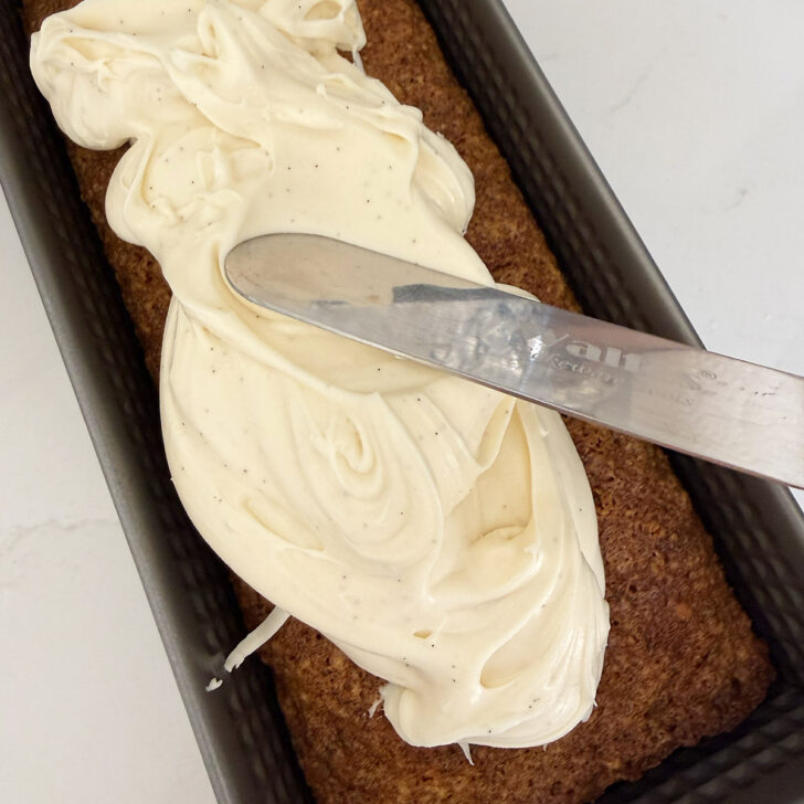 Spreading the cream cheese frosting on the cooled carrot cake loaf.