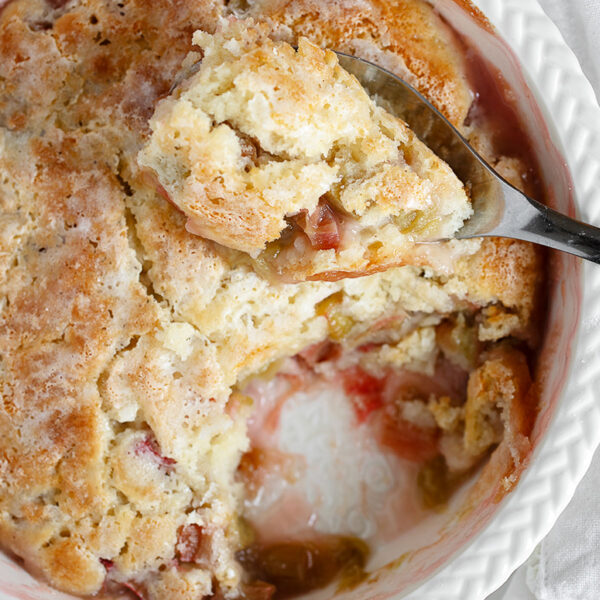 Rhubarb pudding cake in baking dish with spoon.