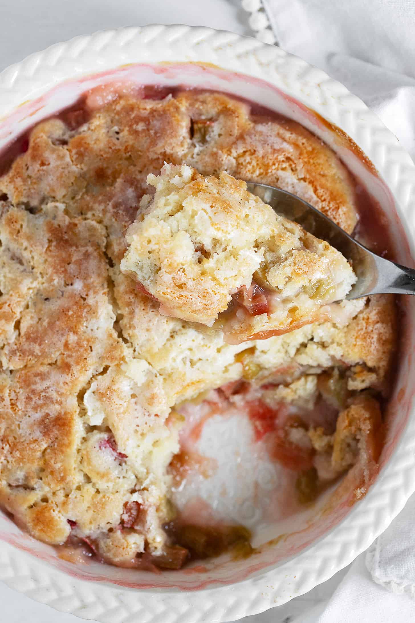 Rhubarb pudding cake in baking dish with spoon.