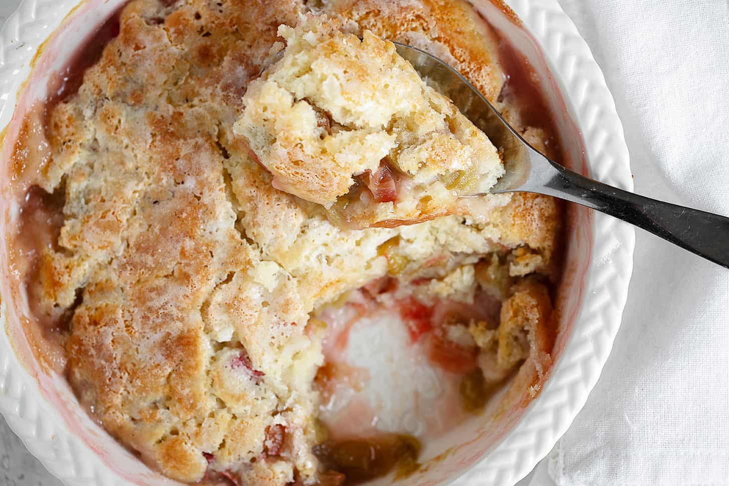 Rhubarb pudding cake in baking dish with spoon.