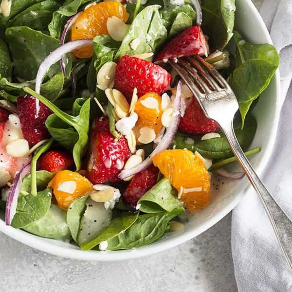spinach strawberry salad in white bowl with fork