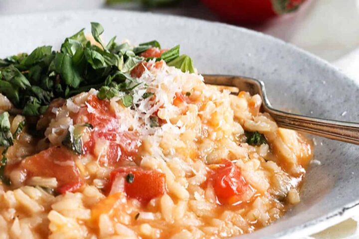 tomato risotto in bowl with whole tomatoes behind
