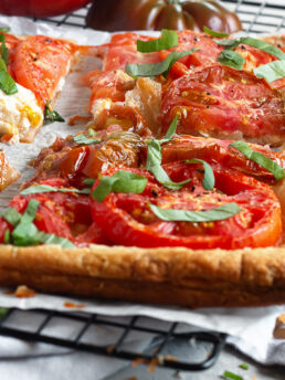 Tomato ricotta puff pastry tart sliced on a parchment-lined cooling rack.