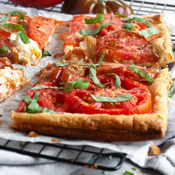 Tomato ricotta puff pastry tart sliced on a parchment-lined cooling rack.