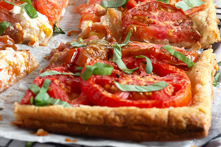Tomato ricotta puff pastry tart sliced on a parchment-lined cooling rack.