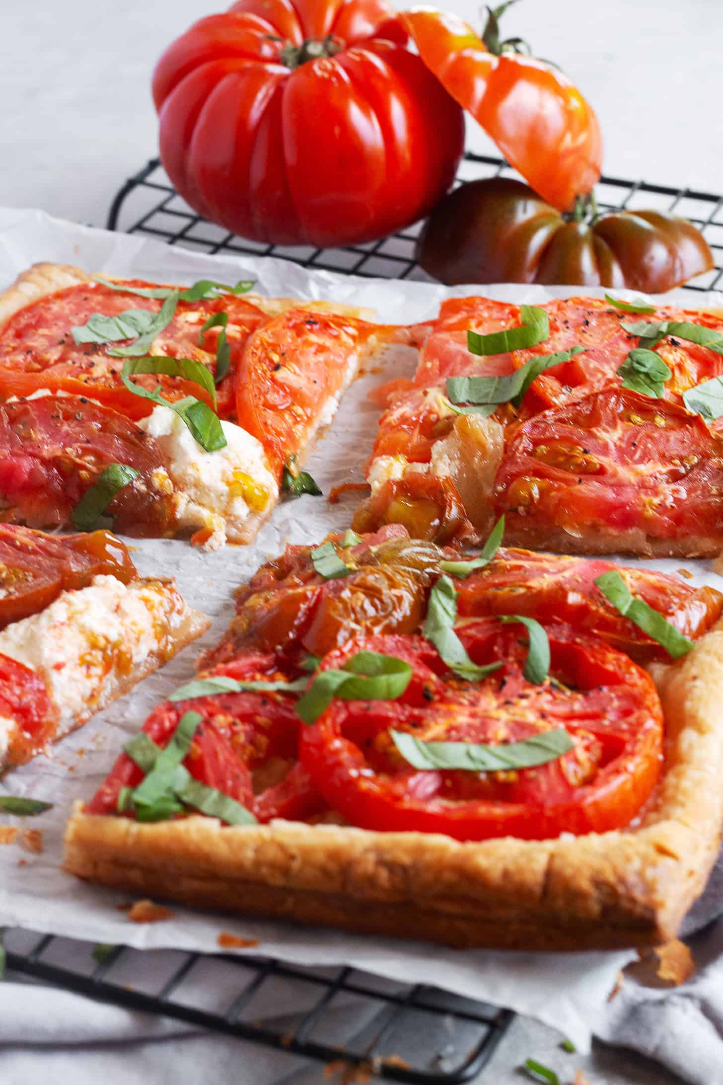 Tomato ricotta puff pastry tart sliced on a parchment-lined cooling rack.