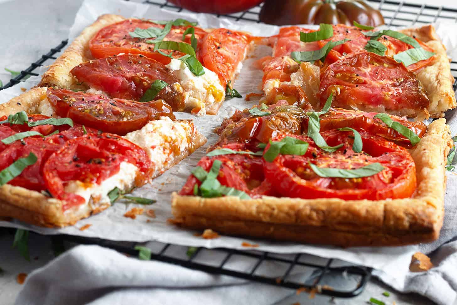 Tomato ricotta puff pastry tart sliced on a parchment-lined cooling rack.