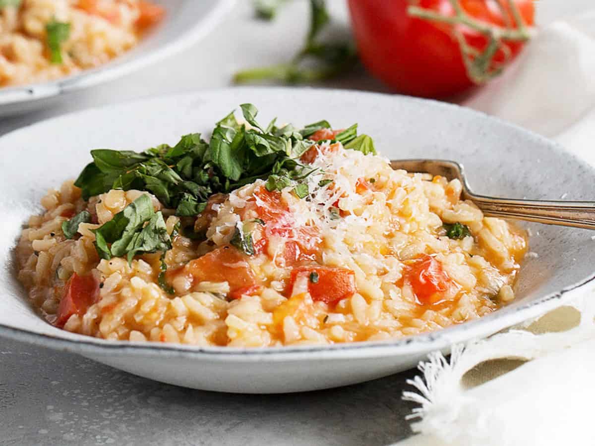 tomato risotto in bowl with whole tomatoes behind