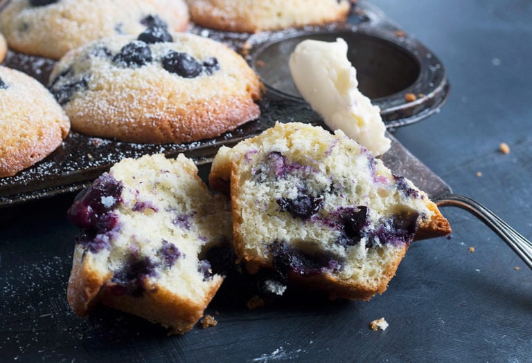 blueberry lemon muffins in muffin tin with one sliced