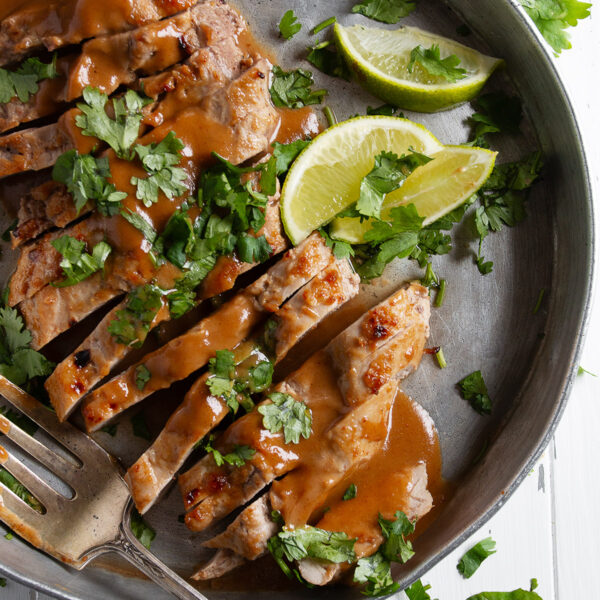 Pork tenderloin with peanut sauce on a serving platter with limes.