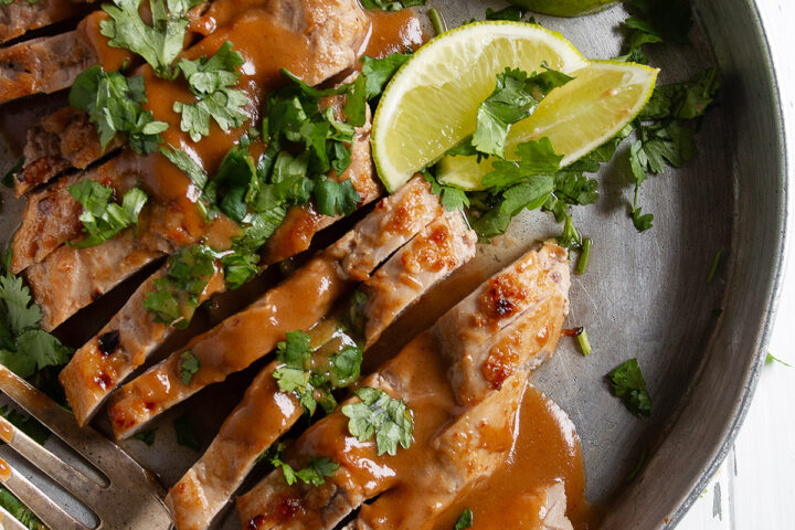 Pork tenderloin with peanut sauce on a serving platter with limes.
