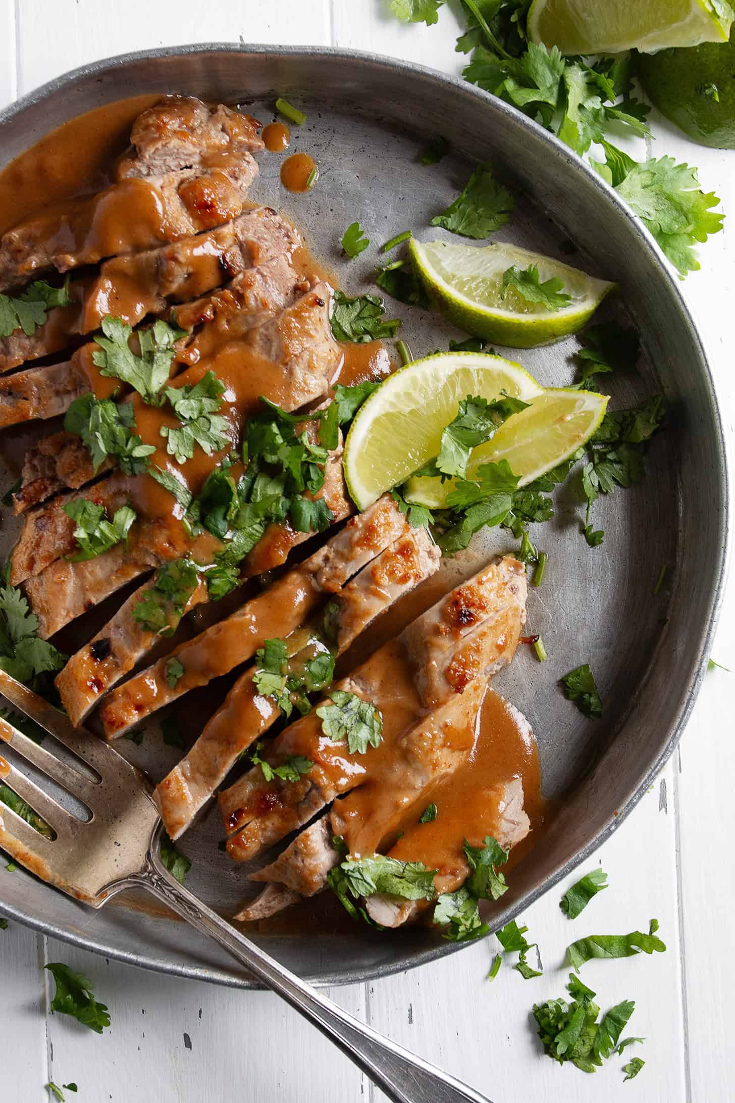 Pork tenderloin with peanut sauce on a serving platter with limes.