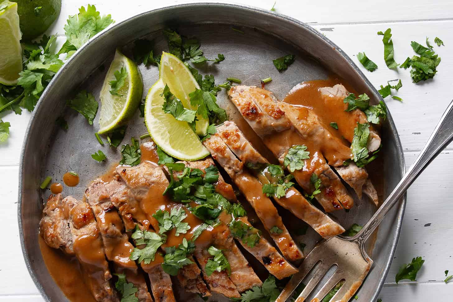 Pork tenderloin with peanut sauce on a serving platter with limes.