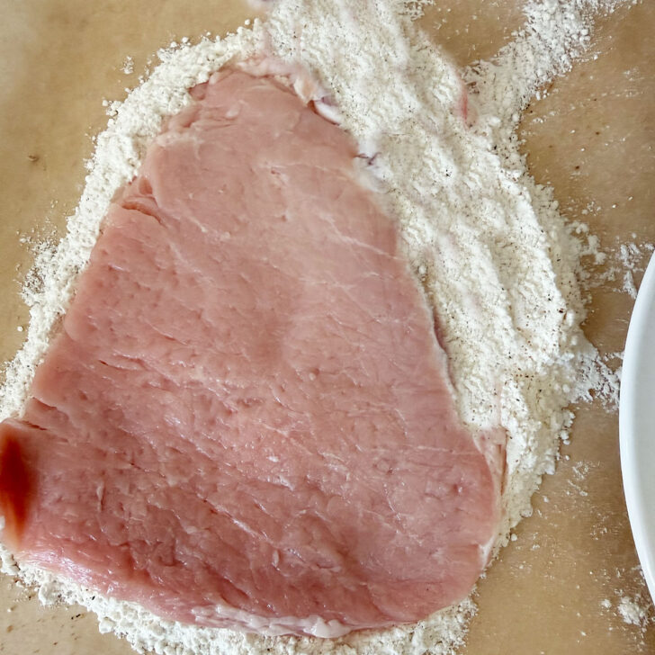 Dredging the pork in seasoned flour.