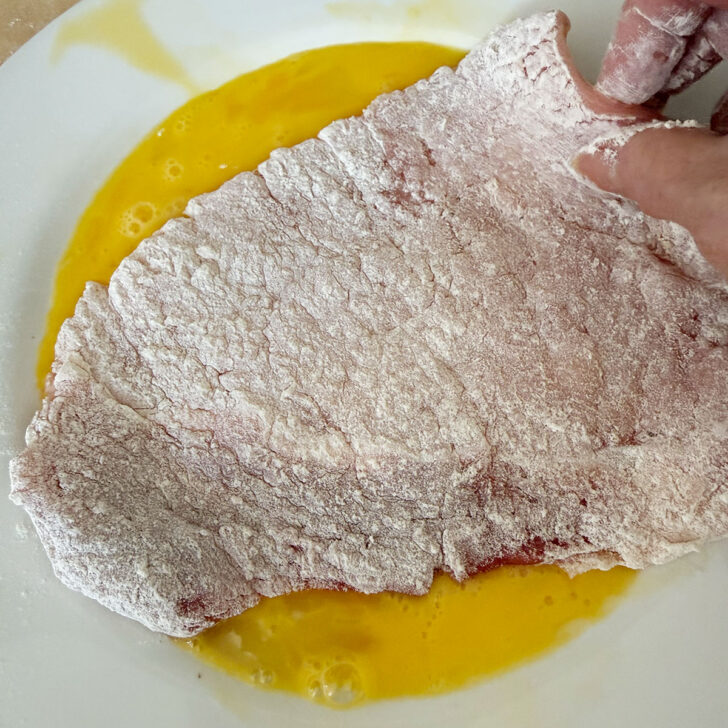 Dipping the floured pork into beaten egg.