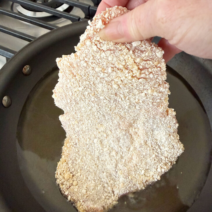 Adding the chilled, breaded pork schnitzel to hot oil in a skillet.