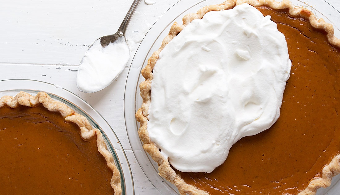 pumpkin pie being topped with whipped cream