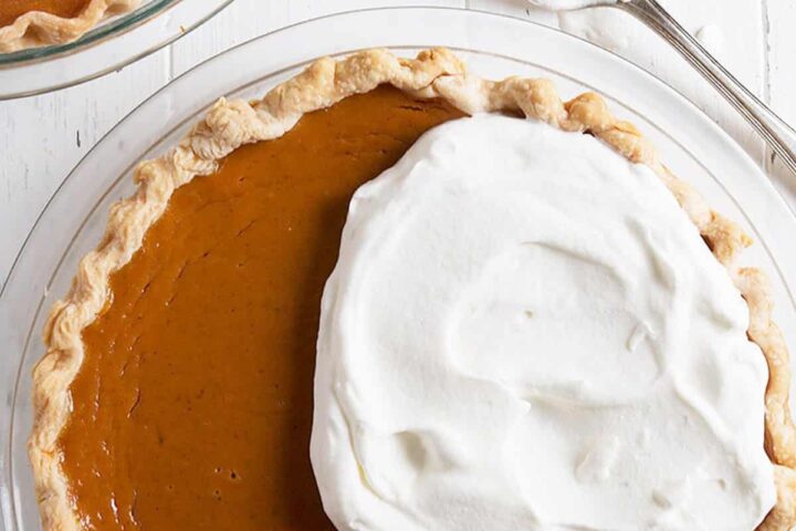 pumpkin pie being topped with whipped cream