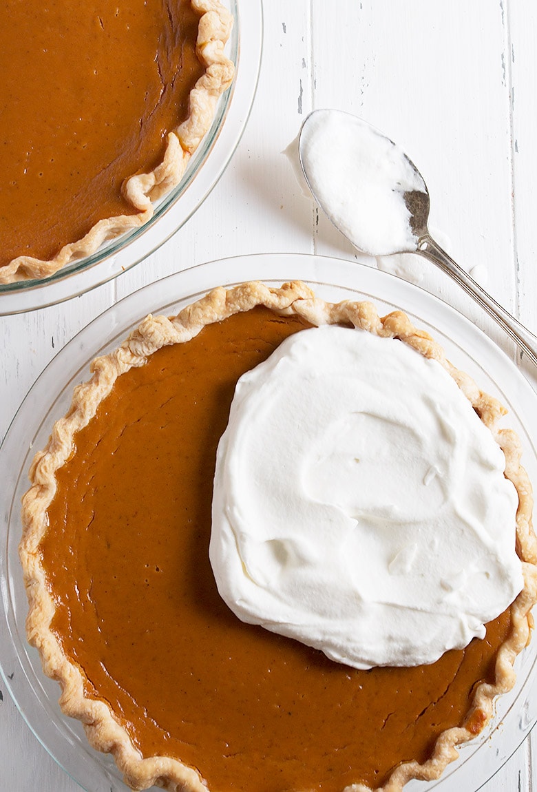 pumpkin pie being topped with whipped cream