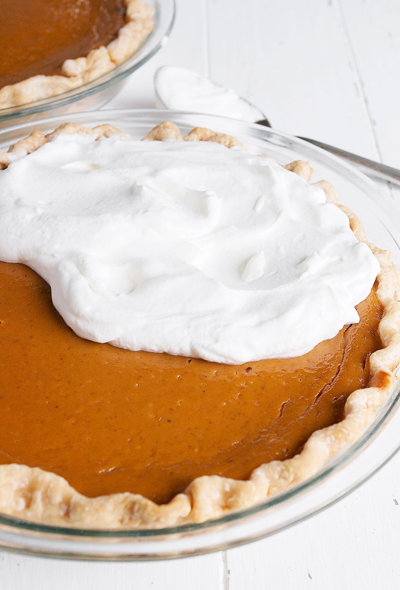 pumpkin pie being topped with whipped cream