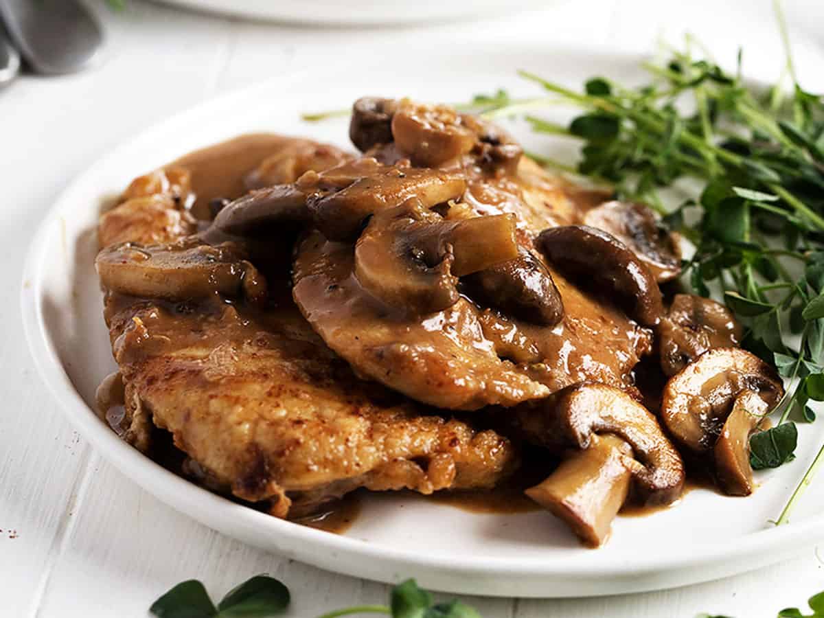 chicken marsala on white plate with green sprouts