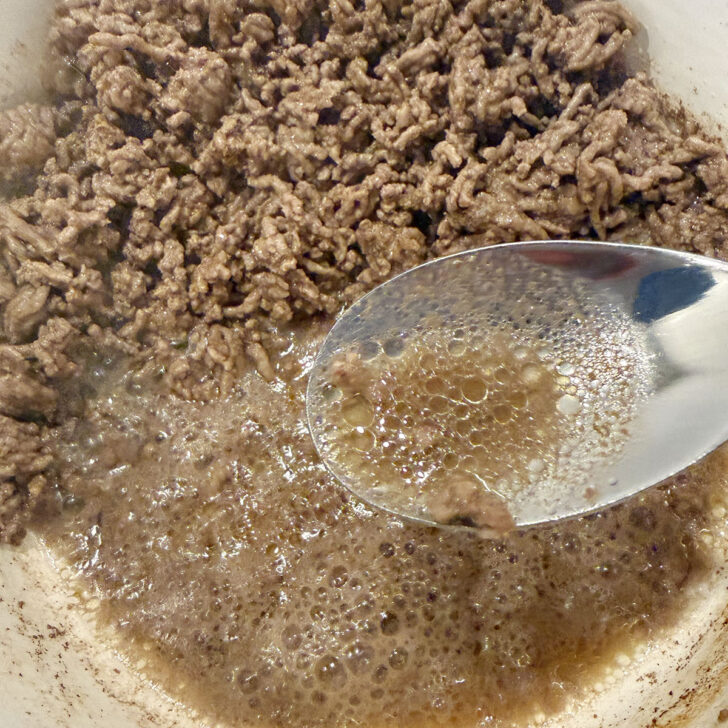 Spooning the excess fat out of the pot after browning the ground beef.