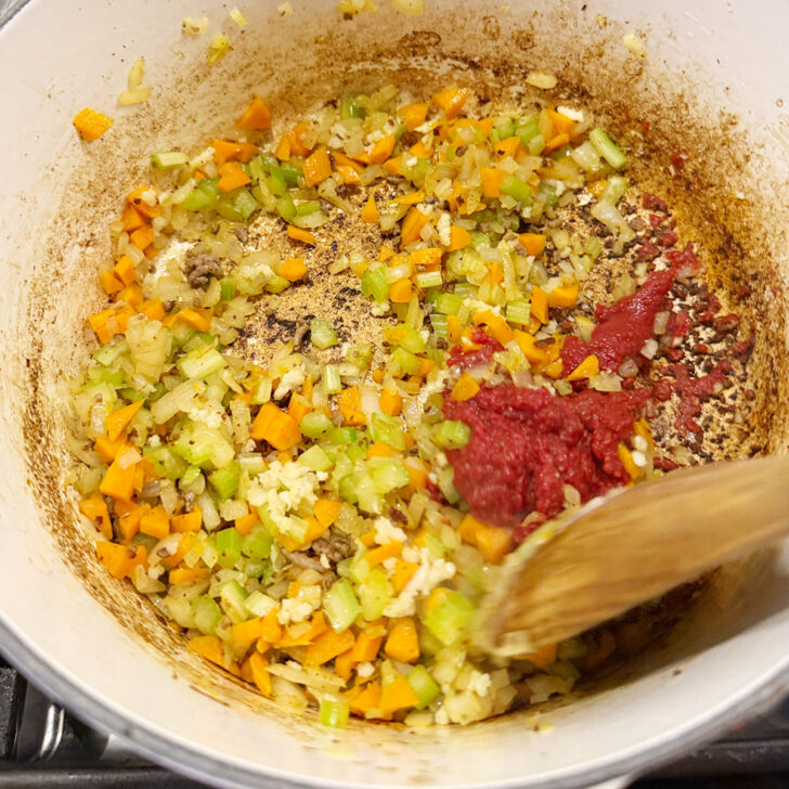 Adding tomato paste to the pot after cooking the vegetables.