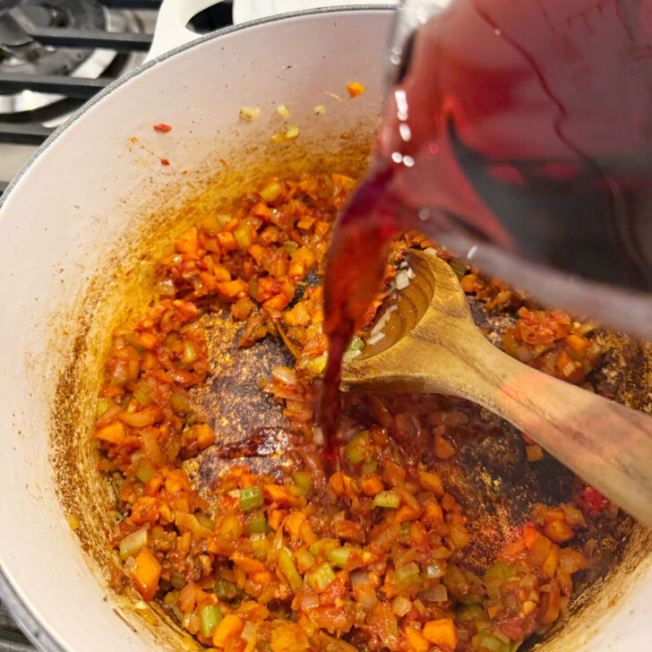 Adding red wine to the pot with the vegetables.