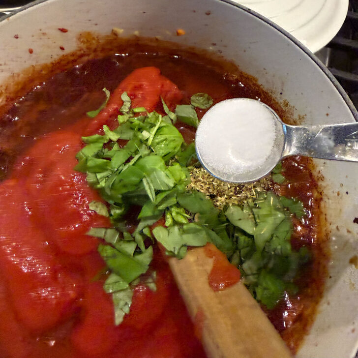 Tomatoes, basil, herbs and salt added to the pot.