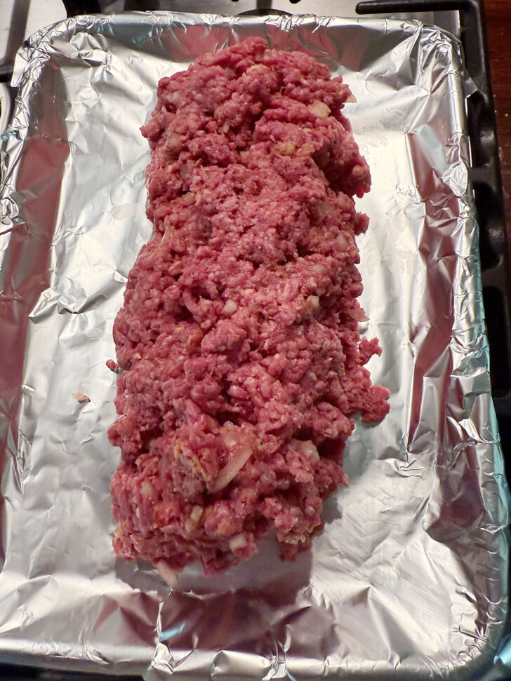 Meatloaf mixture spooned onto a foil-lined baking sheet.