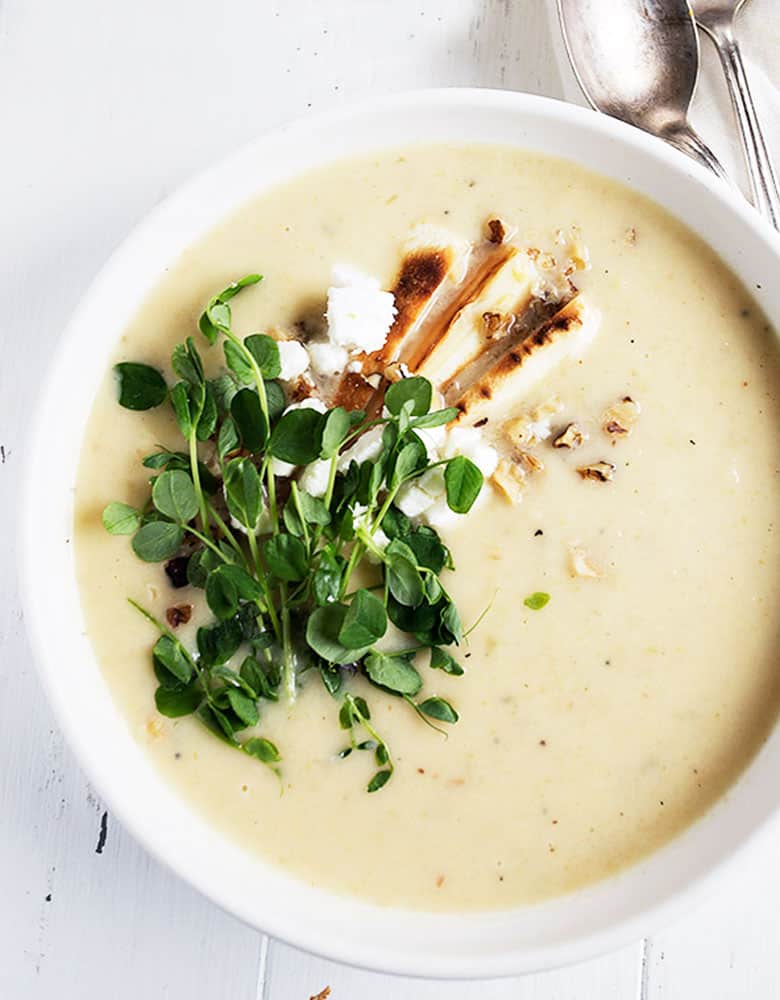 parsnip and pear soup in white bowl with garnishes on top