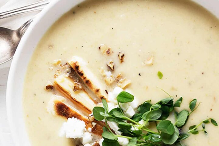 parsnip and pear soup in white bowl with garnishes on top