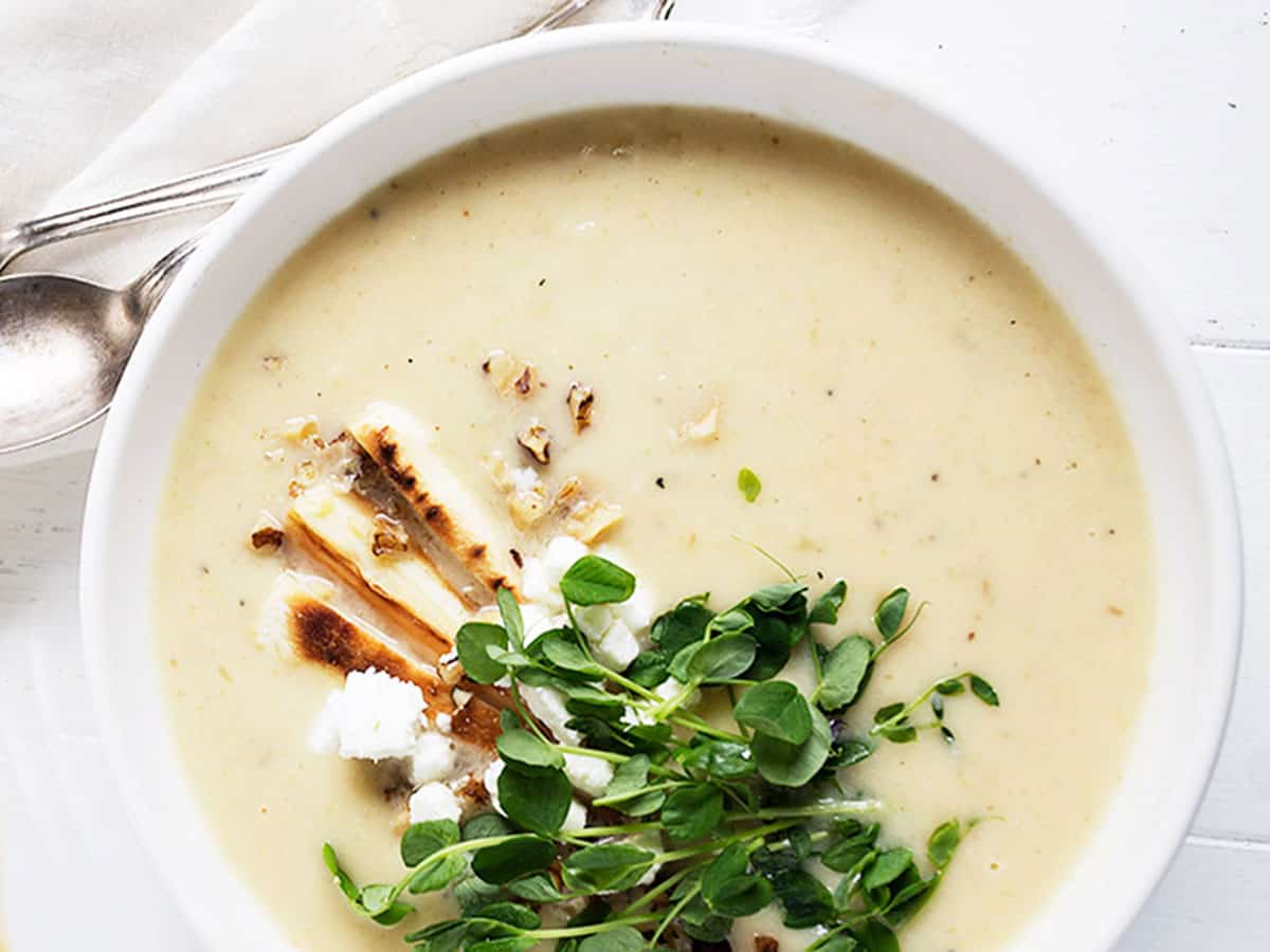 parsnip and pear soup in white bowl with garnishes on top