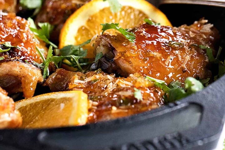 sticky orange chicken in skillet with orange slices