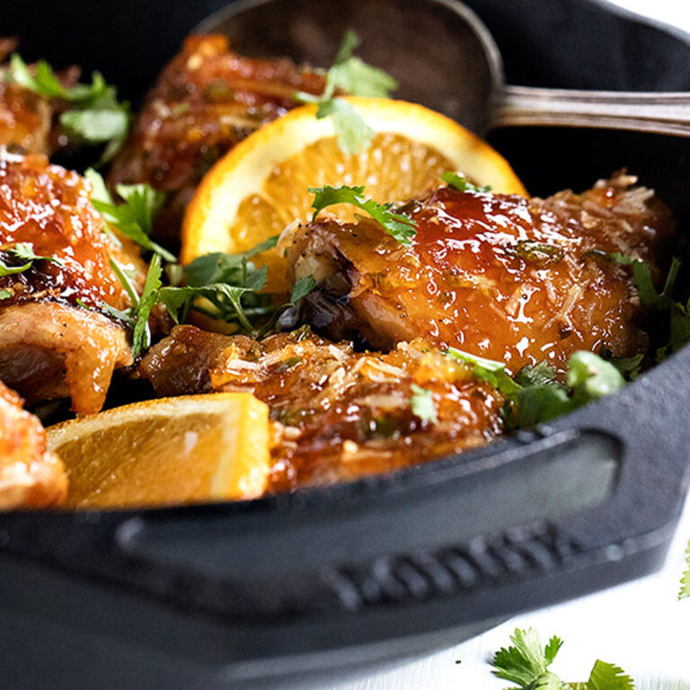 sticky orange chicken in skillet with orange slices