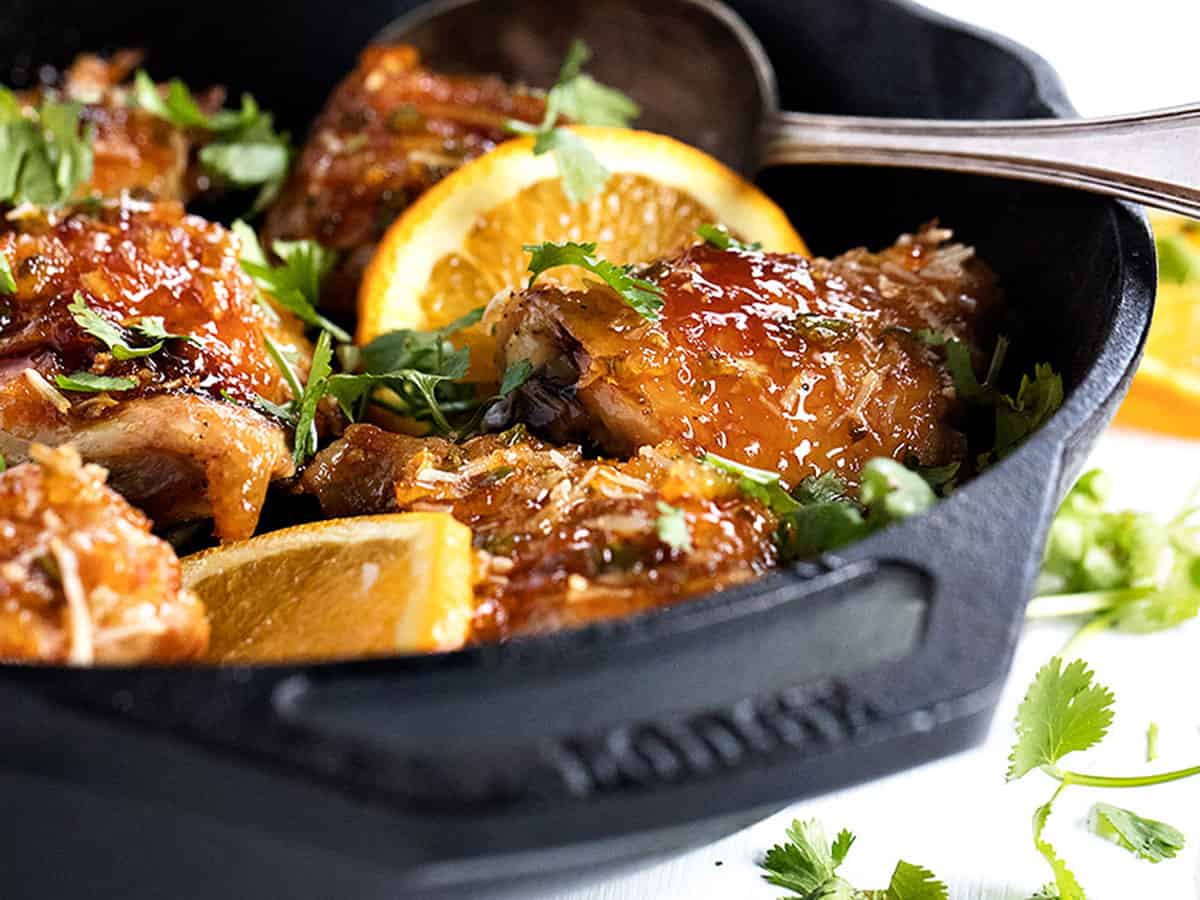 sticky orange chicken in skillet with orange slices