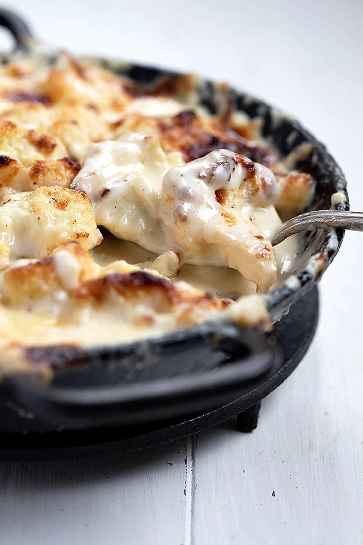 cauliflower cheese in cast iron skillet with spoon