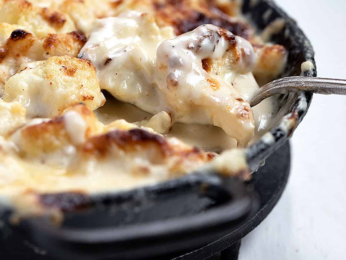 cauliflower cheese in cast iron skillet with spoon