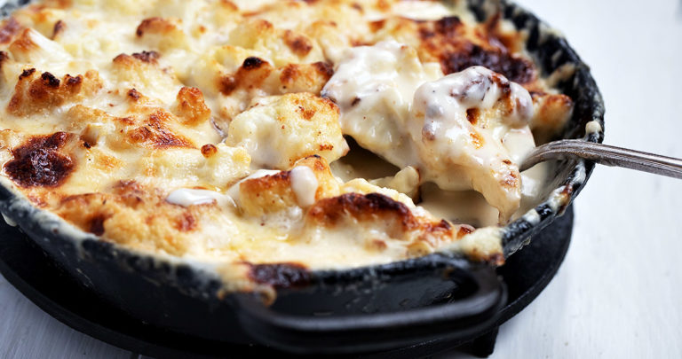 cauliflower cheese in cast iron dish with spoon