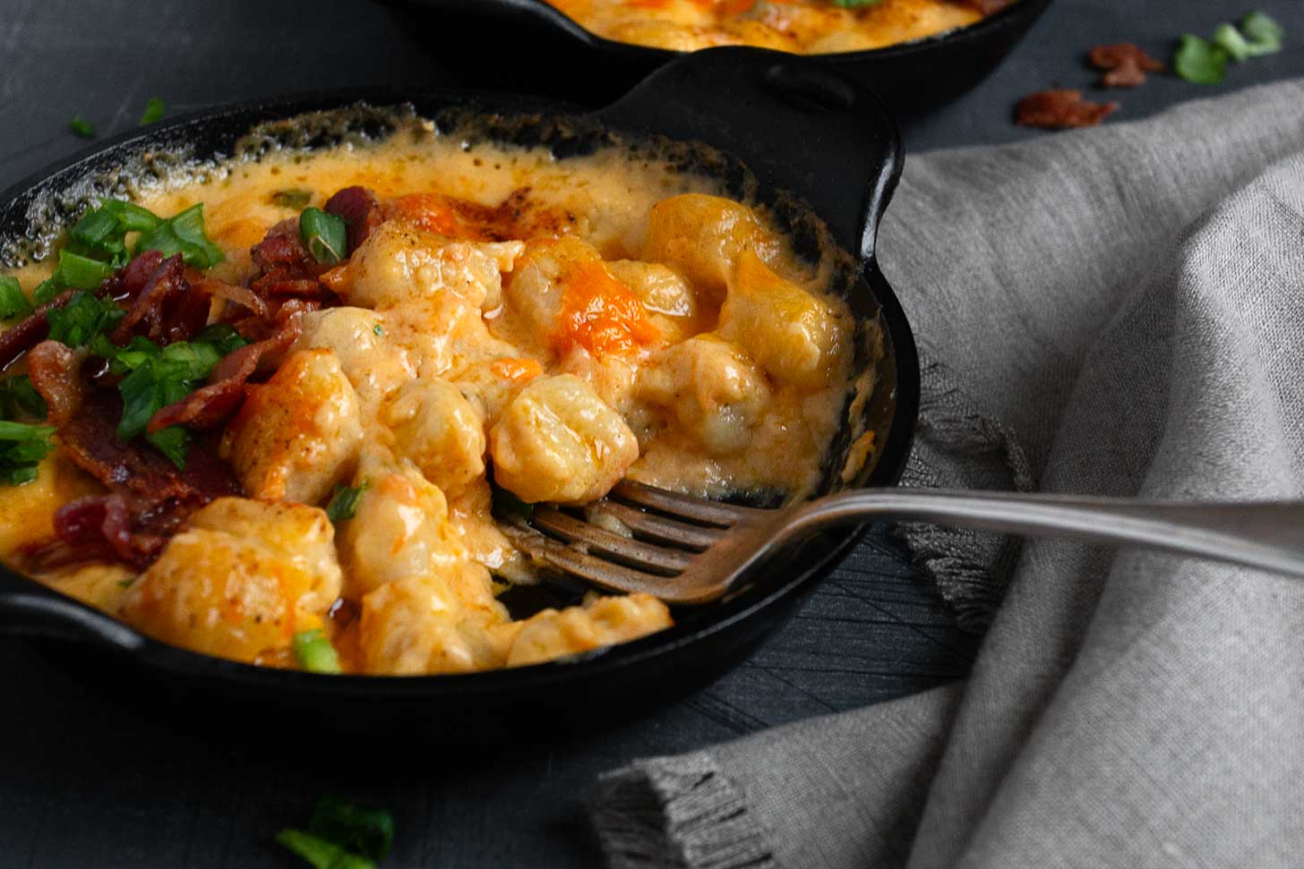 Cheesy baked gnocchi in cast iron skillets with fork.