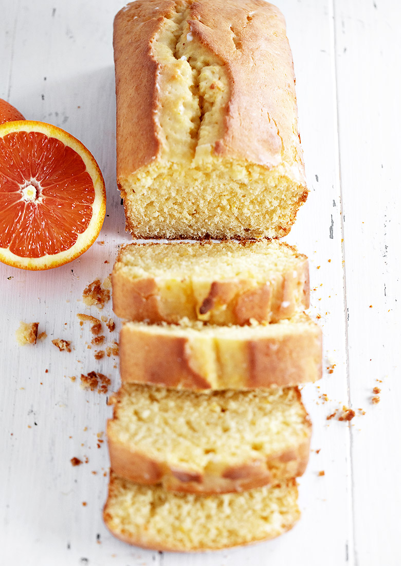 orange pound cake loaf sliced on white background with orange half