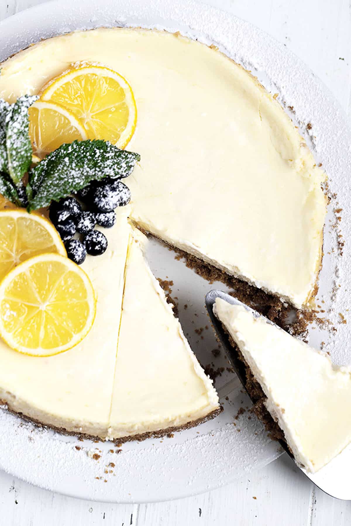 lemon cheesecake cut on plate with berries and lemon slices on top