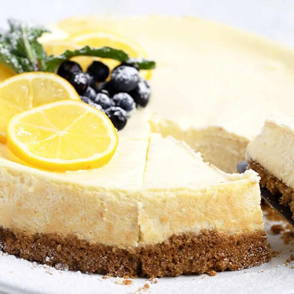 lemon cheesecake cut on plate with berries and lemon slices on top