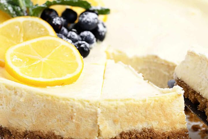 lemon cheesecake cut on plate with berries and lemon slices on top
