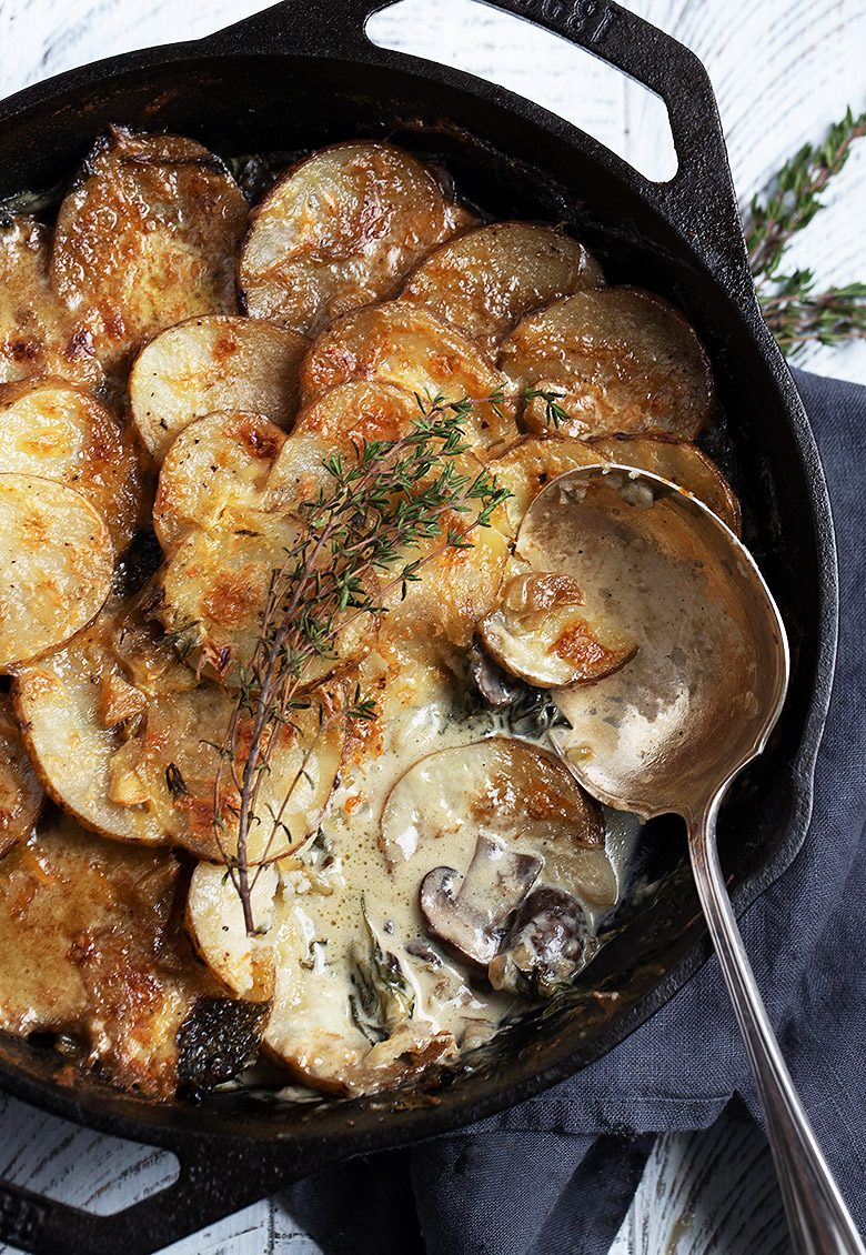 cheese topped potato slices and mushrooms in a cast iron skillet